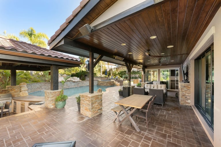 A luxury outdoor living space with covered patio, pool, lush landscaping, and stone accents