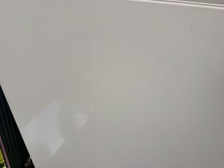 Blurry photograph of a light gray ceiling or wall with partial view of black trim on the left edge