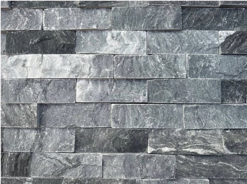 Close-up of stacked stone tile wall with varying shades of gray and black in a brick-like pattern