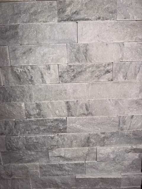 Gray stone tiles arranged in a staggered brick pattern on a wall, showing natural texture and veining