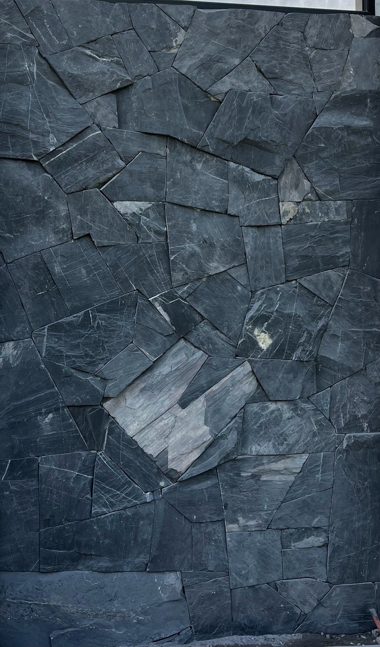 Irregular dark gray slate tiles arranged in an abstract mosaic pattern on a wall surface.