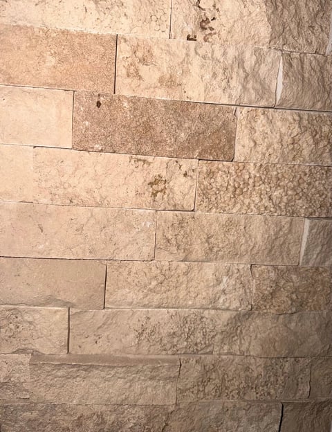 Staggered pattern of light tan and beige stone tiles with visible grout lines and textured surfaces