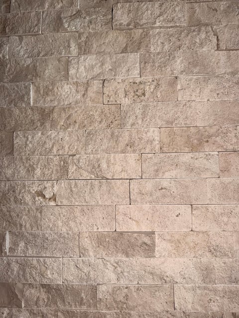 Close-up of beige and tan stone tiles in a running bond brick pattern with varying textures and surface finishes