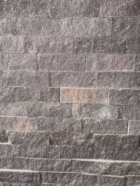 Gray stone tiles with textured surface arranged in staggered rows, forming a modern brick-pattern wall or floor