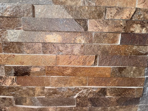 Close-up of stacked stone brick wall with varying shades of brown, tan, and gray in a horizontal running bond pattern