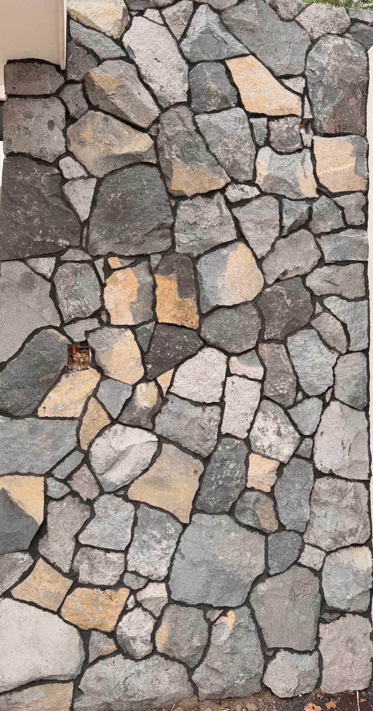 Close-up of irregular stone wall with gray, tan, and beige rocks fitted together with dark mortar joints