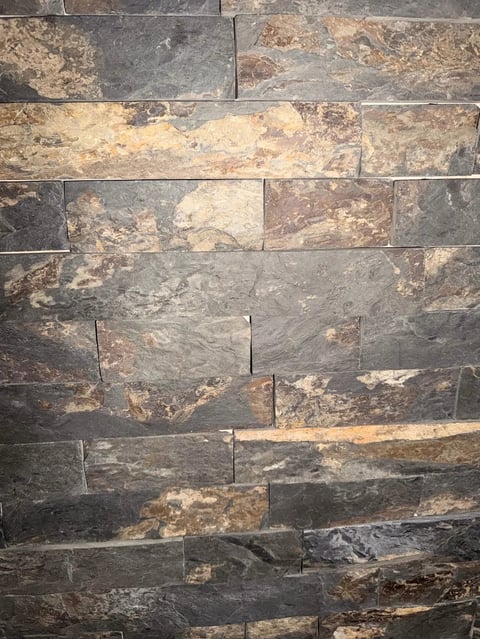 Close-up of stacked stone wall with rectangular tiles in gray, tan, and brown earth tones with natural texture variations
