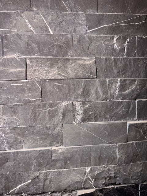 Close-up of gray and black marble tile wall with white veining and varied rectangular brick pattern layout
