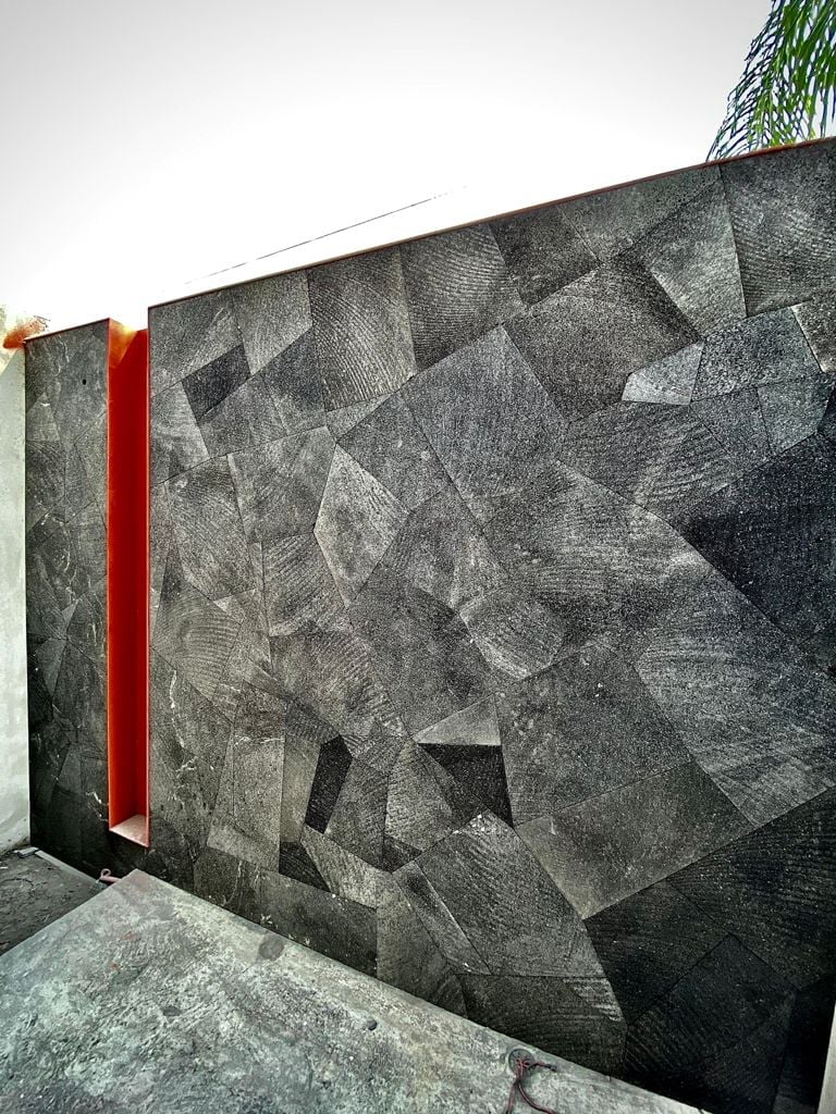 Modern concrete wall with geometric carved patterns and a vertical red stripe accent, palm tree visible above